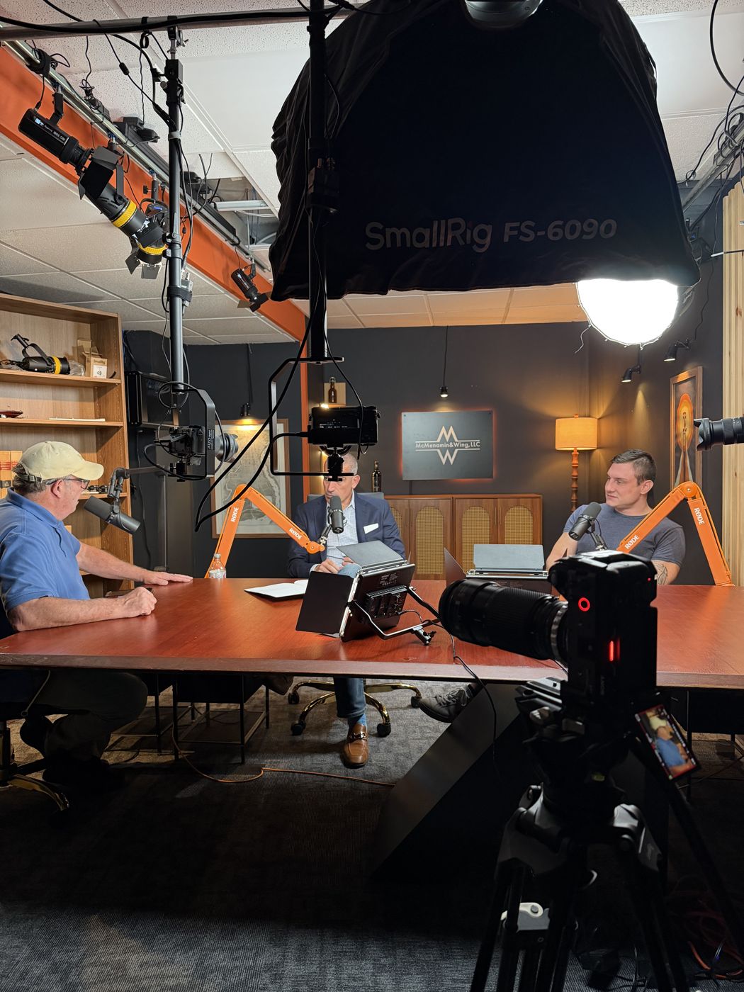 Behind the scenes: overhead lighting rig, three cameras and the hosts at the table in the McMenamin & Wing studio